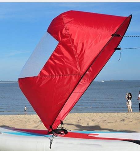 Folding kayak sail with high-visibility PVC window and waterproof fabric, deployed on a kayak by the beach.